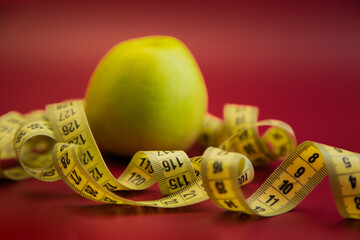 Fresh green apple on a striking red backdrop, entwined with a yellow measuring tape, representing health, nutrition, and the significance of mindful eating habits