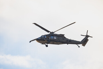 Armed forces helicopter with camouflage fuselage, dual rotor system and tactical airframe design captured in airborne movement beneath light sky
