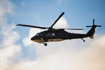 Armed forces rotary aircraft with aerodynamic body, multi-blade rotor system and underbelly equipment captured during steady flight in clear sky