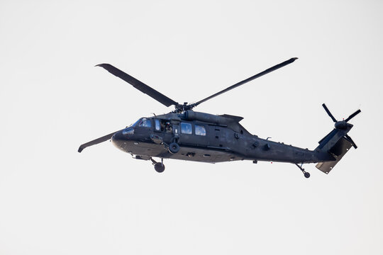 Military utility helicopter in midair with extended landing gear, front sensors and tail rotor visible during flight operation against bright open sky