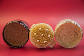 Three jars of body scrubs with unique textures and colors, displayed against a bright red background, highlighting natural skincare and beauty essentials for self-care
