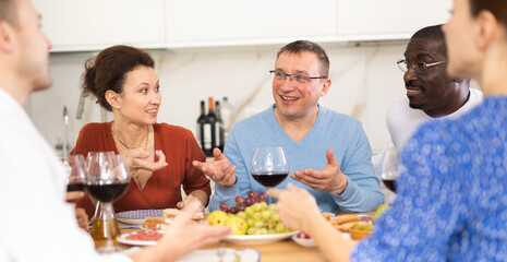 Happy companions congregated around a festive table, participating in animated discussions and enjoying the delights of red wine