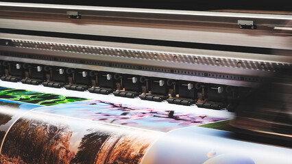 A moving working industrial wide format printer prints a color picture on paper.
