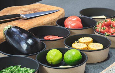 A bowl of vegetables including tomatoes, corn, and lime. A knife is on a cutting board