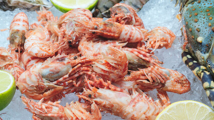 Fresh shrimp, oysters, and limes lie on ice. The shrimp are pink and the limes are green. The seafood is at a market or a market stall.