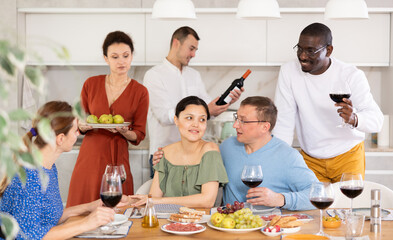Merry male and female friends having wine and talking warmly in comfort of their house, kind lady treating fruit-plate