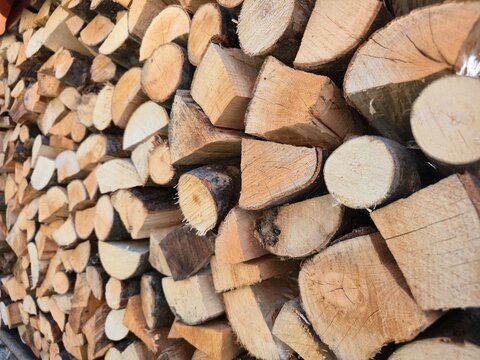 Full frame close-up texture background of a neat stack of light-colored chopped firewood and logs; winter fuel, renewable energy source, natural rustic material, shallow depth of field.