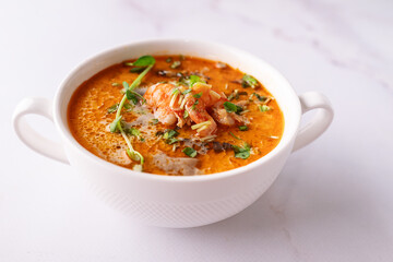 Fresh aromatic hot Thai soup Tom Yum with mushrooms, shrimps and different spices on white marble background close up. Tasty food concept.