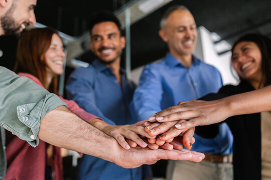 Business team stacking hands in a circle showing unity and support at work. Group celebrating trust and collaboration in a positive environment. Teamwork and achievement concept.