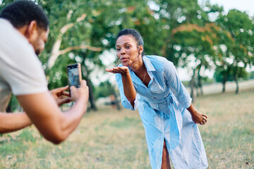 Fototapeta premium Couple having fun outdoors in park or nature taking a photo with a mobile phone, man photographing woman