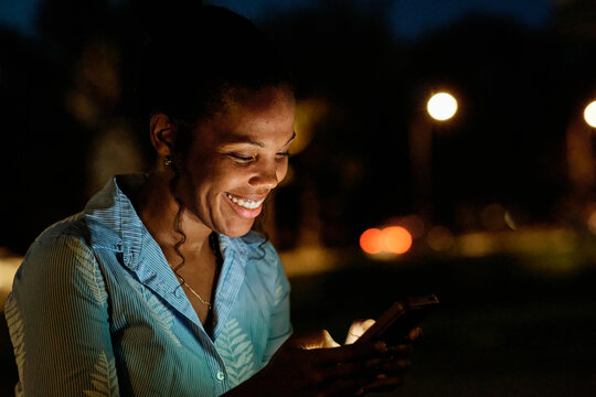 Focused woman using smartphone outdoors during twilight with city lights in the background