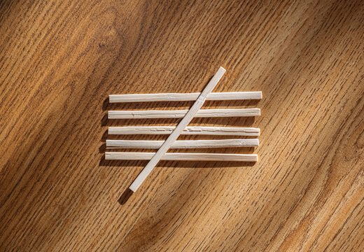 A group of thin wooden tally marks representing the number five is arranged on a highly textured, brown wood surface with dramatic sunlight and shadow. Ideal for business concepts.
