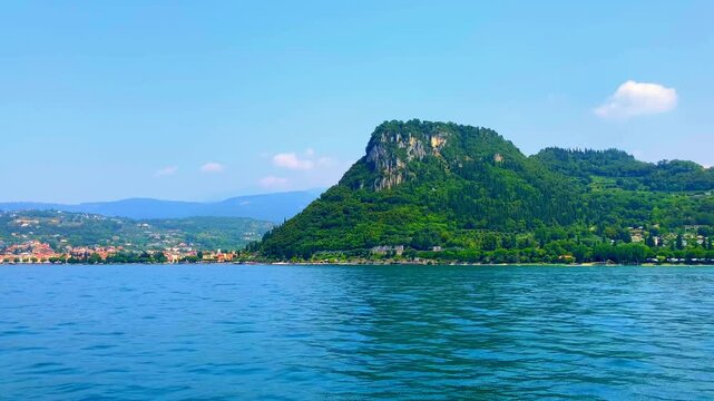 Amazing scene from Lago di Garda with the intersection between Bardolino and Garda crowned by Rocca di Garda, an impressive promontory jutting high from the surrounding green terrain and fluid waters