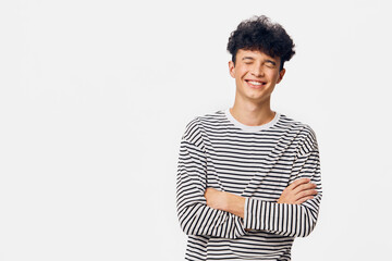 Smiling young man in striped shirt with curly hair stands with arms crossed against white...