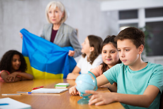 listening to teacher s story about Ukraine, child examines this country on globe
