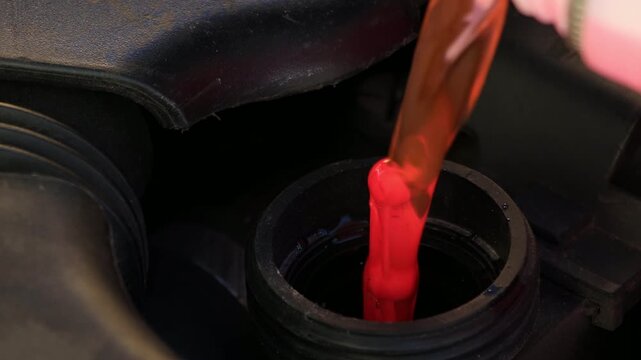 Red coolant is poured into the car&rsquo;s antifreeze reservoir, with a red float rising as the tank fills. Close-up video shows the cooling system being topped up with fresh red antifreeze.