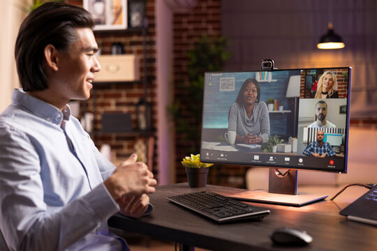 Portrait of young asian entrepreneur seated at desk during online meeting. Male remote worker with cheerful expression, collaborates with colleagues on digital business projects from home office.