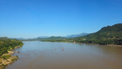 Rural Mountain River Valley View Low Water in laos landscape. Vibrant natural laos landscape featuring lush green mountains stretching across the background beneath a bright, clear blue sky.