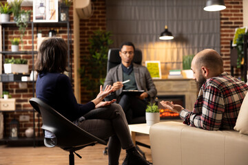 Caucasian boyfriend and girlfriend consult with relationship counselor during therapy session. Young couple sits in therapist office, opening up to professional guidance and seeking marriage support.