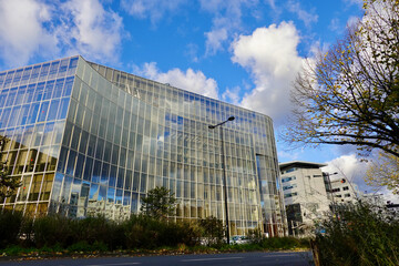Fototapeta premium Contemporary Architectural Marvel Displaying Glass Facade with Blue Sky Reflections and Sparse Vegetation on an Urban Street Setting in Bordeaux