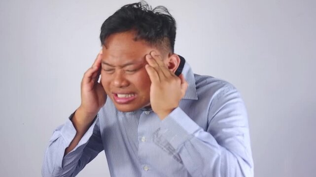 Stressed young Asian man feeling severe headache, Tired and upset man expression massaging temples suffering from migraine isolated on empty gray white studio background. Headache man expression
