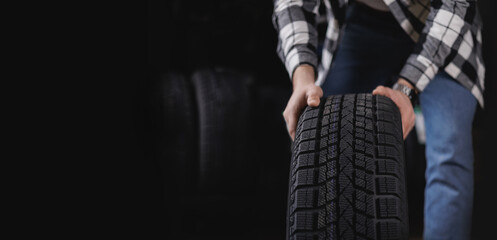 Caucasian male adult handling winter car tire in garage workshop, banner tyre store