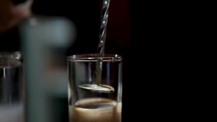 Bartender pours layered cocktail in glass under vibrant bar lighting, steady camera, Bangkok nightlife. High quality 4k footage