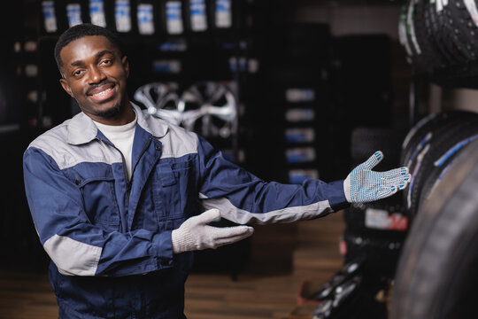 Portrait Happy African male adult mechanic presenting tires in auto repair shop