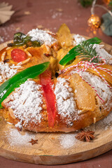 Colorful candied fruits and powdered sugar on a traditional Bolo Rei or Kings Cake, set on a wooden board amidst warm holiday decorations and lights. Is tradicional for Christmas in Portugal
