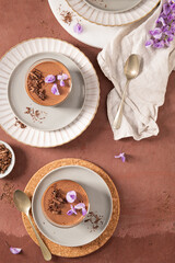 An overhead view of two delicious chocolate mousses in glasses, styled on plates with spoons and garnishes, a sweet presentation.