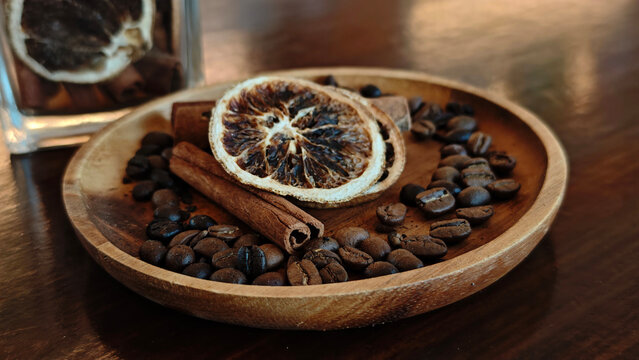 Coffee beans, cinnamon sticks, dried blood oranges on a wooden plate, herbs in a coffee shop.