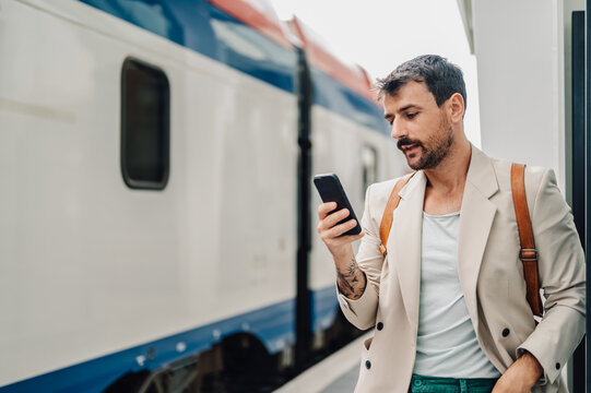 Man commuting to work, checking smartphone on train platform