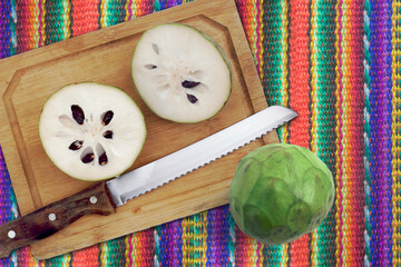 Top view Green Custard Apple fruits on a wooden cutting board, placed on a Colorful background of traditional textile fabric, ready to prepare a delicious juice or a creamy ice cream