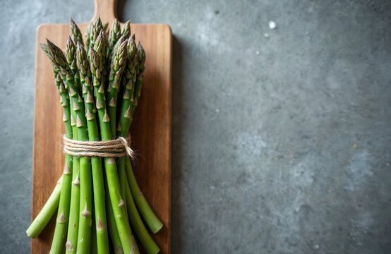 Fresh green asparagus stalks tied with twine rest on a wooden cutting board. The raw vegetables await preparation for a healthy meal. This organic ingredient is perfect for spring recipes.