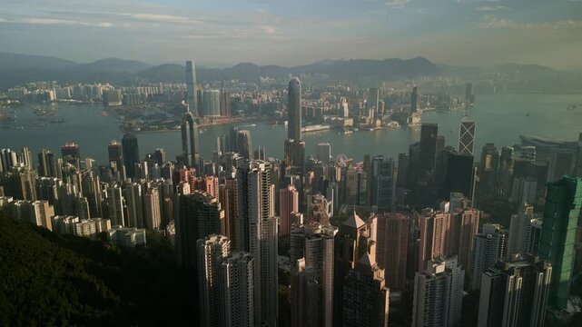 Clear daylight reveals harbour and clustered towers. IFC landmark silhouettes and distant commerce centre rise above crowded streets while ferries mark routes in Hong Kong
