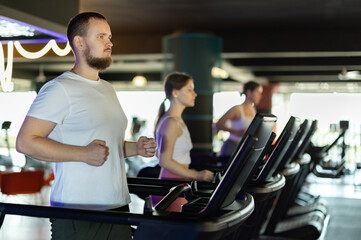 Obraz premium Young athletic man in sportswear training by running on treadmill in gym