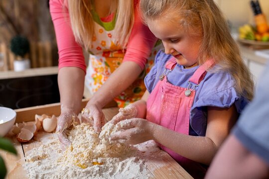 Junior and mother create pastry together, Young child learning baking from nurturing parent, Smiling kid kneading bread alongside caring mother in rustic kitchen
