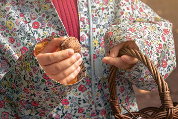 Nahaufnahme eines Kindes in bunter, floral gemusterter Jacke, das einen braunen Weidenkorb mit...