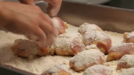 A chef carefully preparing chicken, dusting them with flour