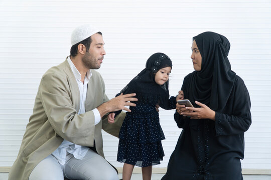 Muslim family spending time together at home. Father, mother, and daughter wearing traditional clothing share a moment of conversation and connection smartphone. Islamic lifestyle technology concepts.