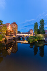 Fototapeta premium Old Town at Evening Twilight. Weinstadel Building, Henkerbrucke Bridge and Henkerturm Tower. Pegnitz River. Reflection in Water. Nuremberg, Franconia, Germany. Wide Shot