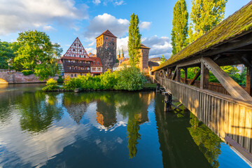 Fototapeta premium Old Town of Nuremberg. Weinstadel Building, Henkerbrucke Bridge and Henkerturm Tower on Summer Sunny Evening. Pegnitz River. Reflection in Water. Franconia, Germany. Wide Shot