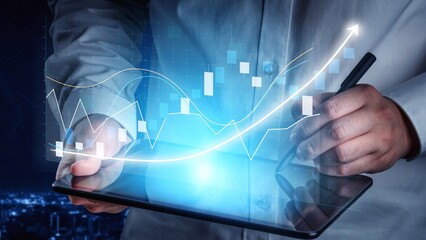 A business professional analyzes financial trends on a digital tablet, surrounded by glowing graphs in a modern nighttime environment, showcasing technology and innovation. Copula