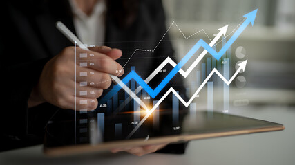 A business professional analyzes financial data on a tablet using a digital pen. The image features rising graphs and charts, symbolizing growth and success. Scalp