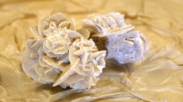 Stone sand rose is rotating against the beige textured background from handmade craft paper, stone illumination, slow motion