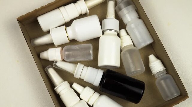 Pile of empty vial of medical drops are in a container for disposal, top view, rotation. Treatment and medication concept