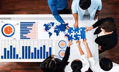 A diverse team collaborates on data analysis using a modern dashboard while assembling puzzle pieces, symbolizing teamwork and strategy in a professional office setting. Axiom