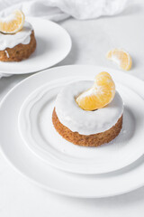 Mini bundt cakes covered in a white glaze on a white countertop, small vanilla bundt cake with a white glaze and tangerine segment on a white background