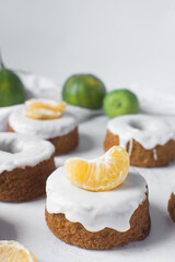 Mini bundt cakes covered in a white glaze on a white countertop, small vanilla bundt cake with a white glaze and tangerine segment on a white background