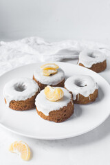 Mini bundt cakes covered in a white glaze on a white countertop, small vanilla bundt cake with a white glaze and tangerine segment on a white background